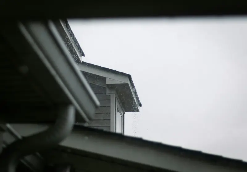 Roofline gutter and downspout against a gray sky