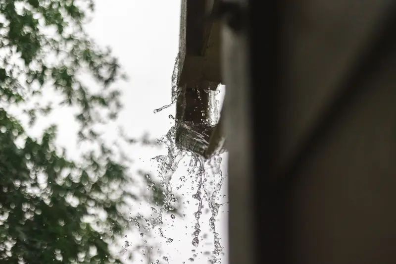 Rainwater pouring from the end of a gutter during a storm